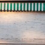A storefront with a green-and-white striped awning and a closed metal shutter, indicating that the business had been shut down.