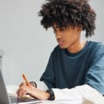 A teenage male, looks at his laptop suggesting he is a young entrepreneur creating a new business.