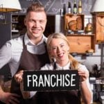 Smiling cafe owners holding franchise sign.
