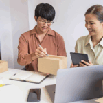 Two people packaging boxes with tablet and laptop.